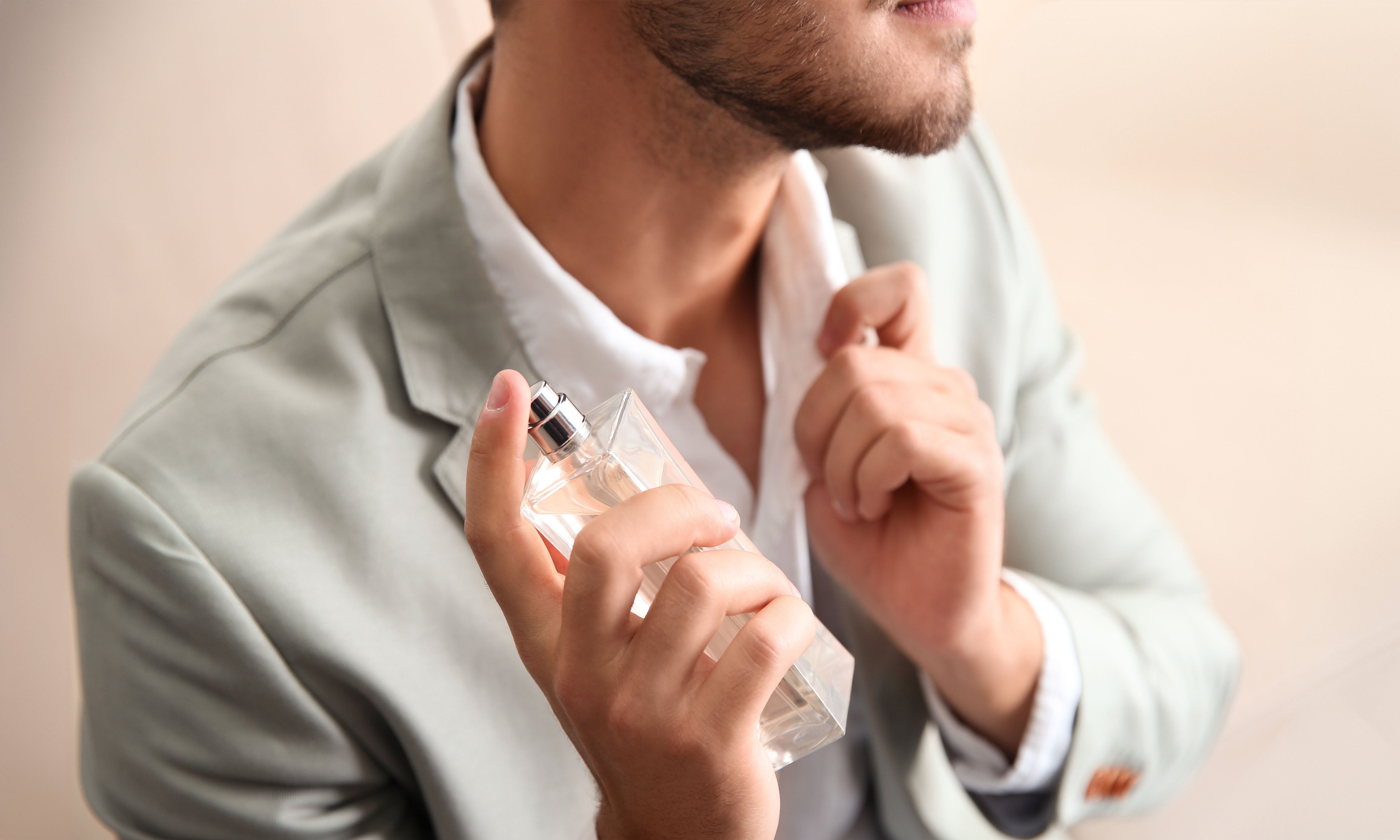 Photographie qui illustre une deuxième manière de se parfumer. Image d’un homme en train de vaporiser du parfum sur sa chemise. Le contexte est simple avec un arrière-plan flou qui met en valeur l'action principale.