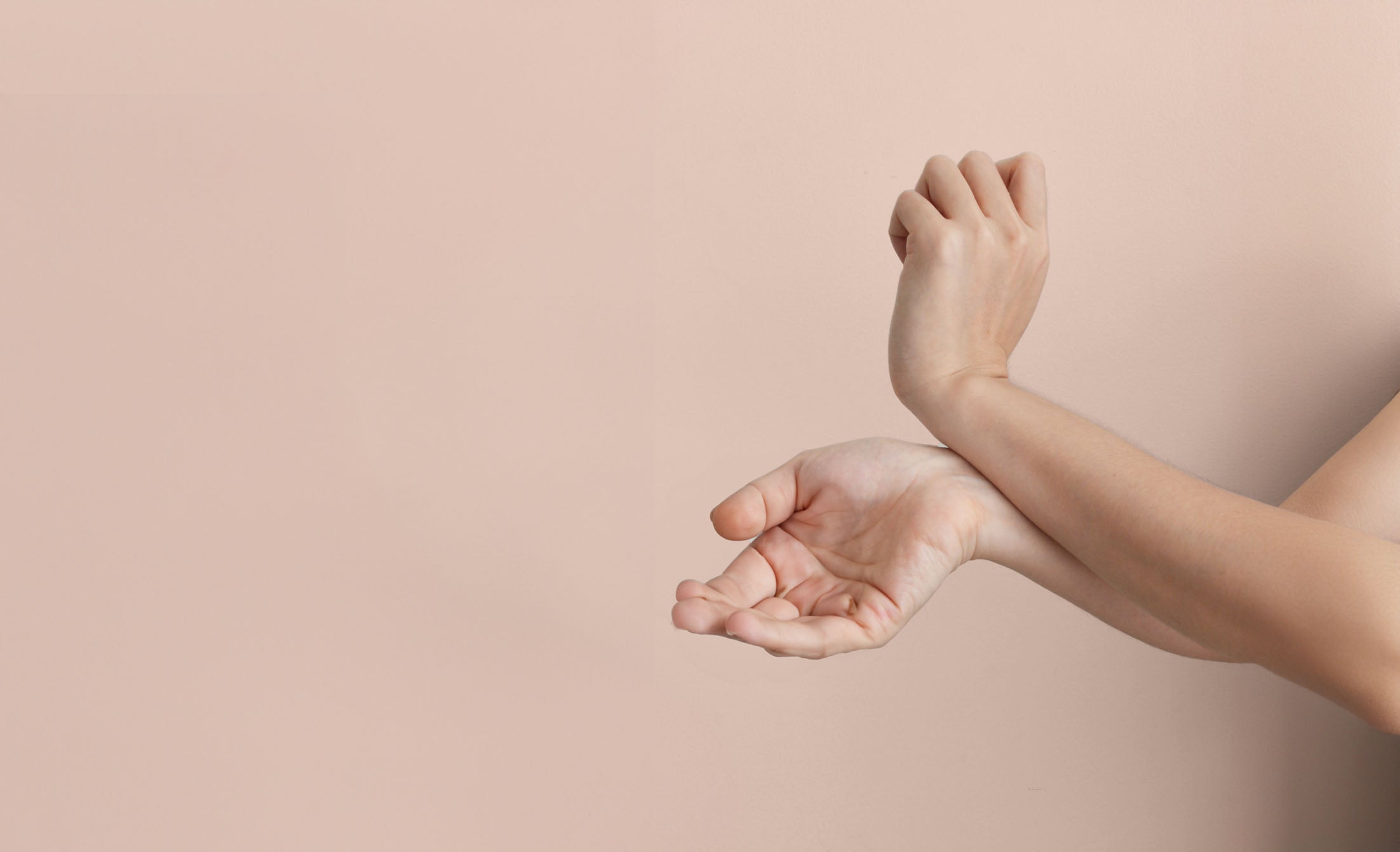 Photographie montrant une personne frottant ses poignets l'un contre l'autre. Les bras sont en position croisée, avec un poignet reposant dans la paume de l'autre main. Le fond de l'image est uni et de couleur neutre, mettant l'accent sur le geste des mains à éviter lorsque l’ont souhaite se parfumer.