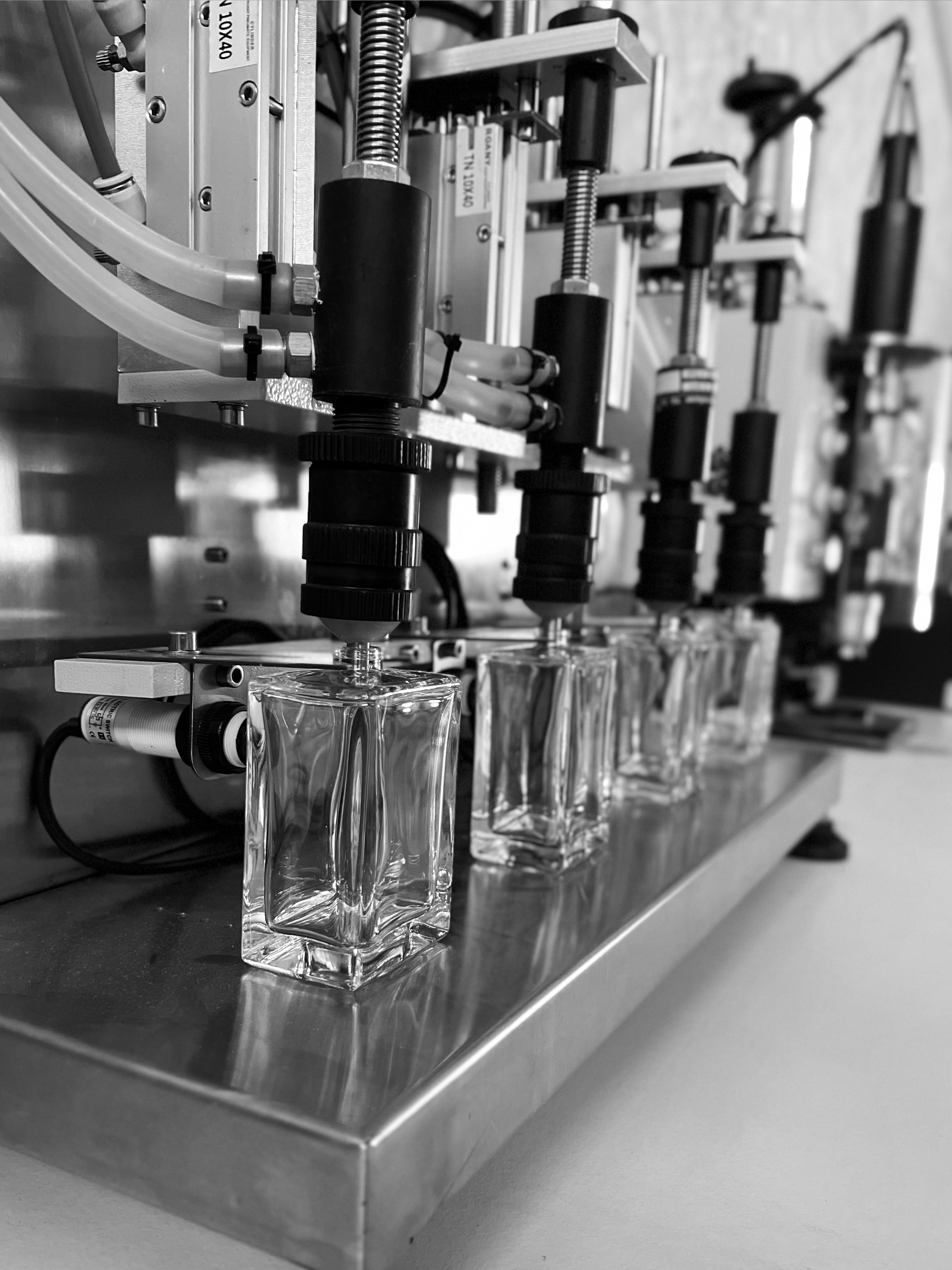 Photographie en noir et blanc illustrant une série de bouteilles de parfum transparentes alignées de la chaîne de production d’Anthèse Manufacture.